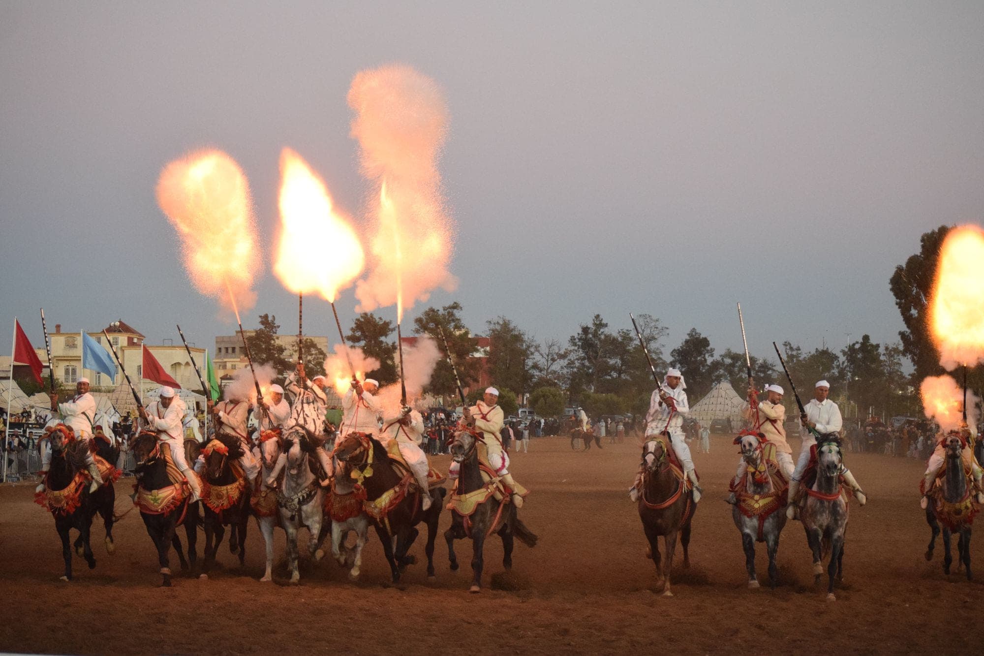 Cavaliers marocains en tenue traditionnelle exécutant une fantasia au crépuscule