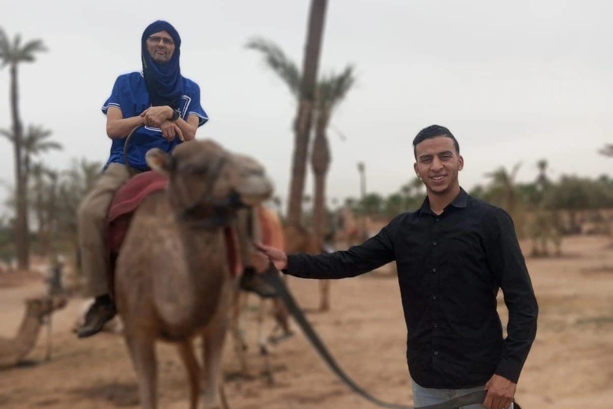 Client à dos de dromadaire dans la palmeraie de Marrakech, accompagné d'un guide qui tient la longe
