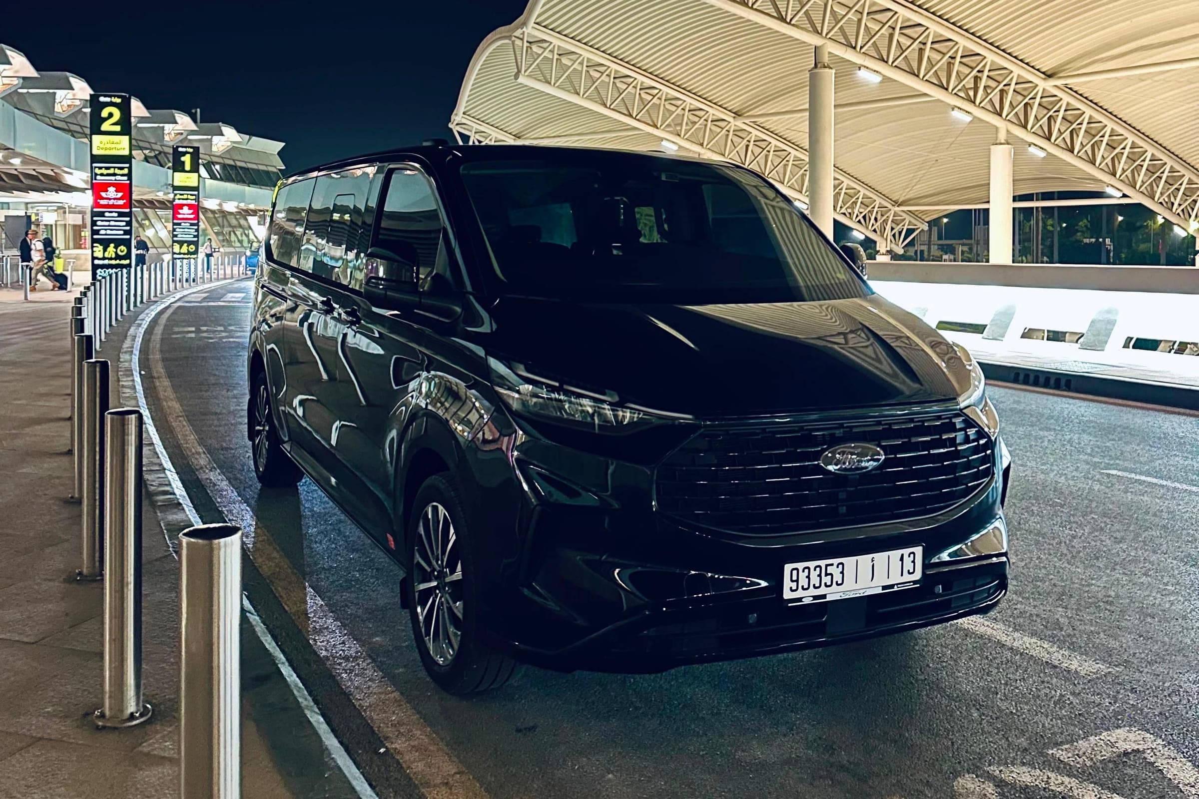 Ford Tourneo noir de Morocco Travel Transfr stationné de nuit devant le terminal départs d'un aéroport marocain