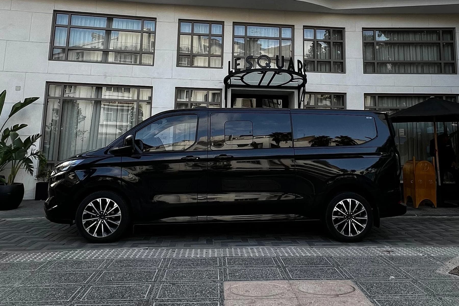 Ford Tourneo noir vu de profil, à l'arrêt devant l'entrée d'un hôtel
