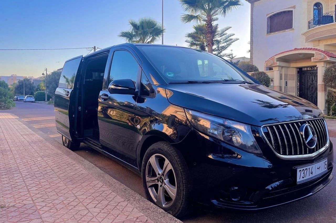 Mercedes-Benz Vito noir, porte latérale coulissante ouverte, dans une rue bordée de palmiers en fin de journée