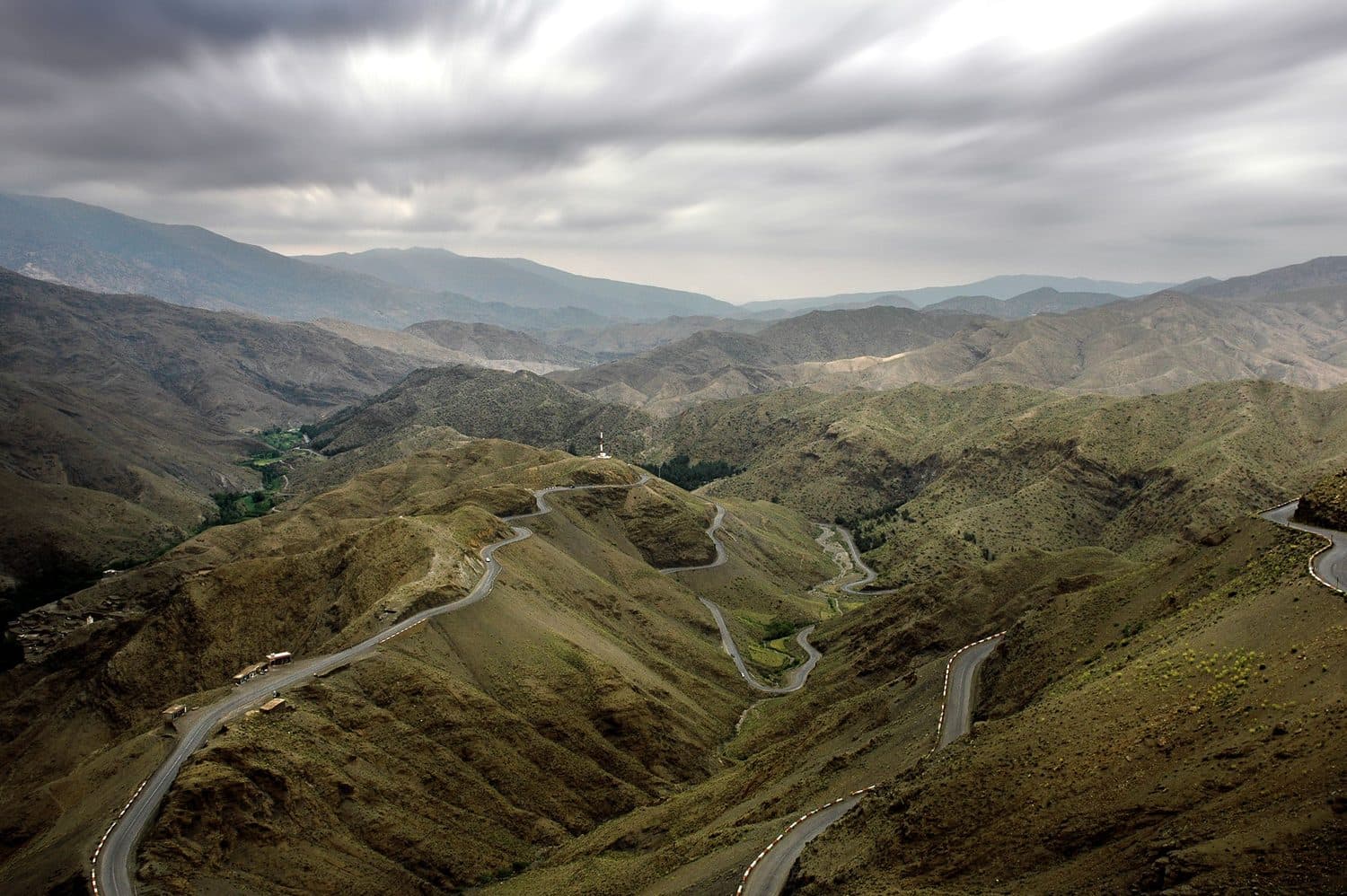 Route sinueuse traversant les collines verdoyantes de l'Atlas sous un ciel couvert